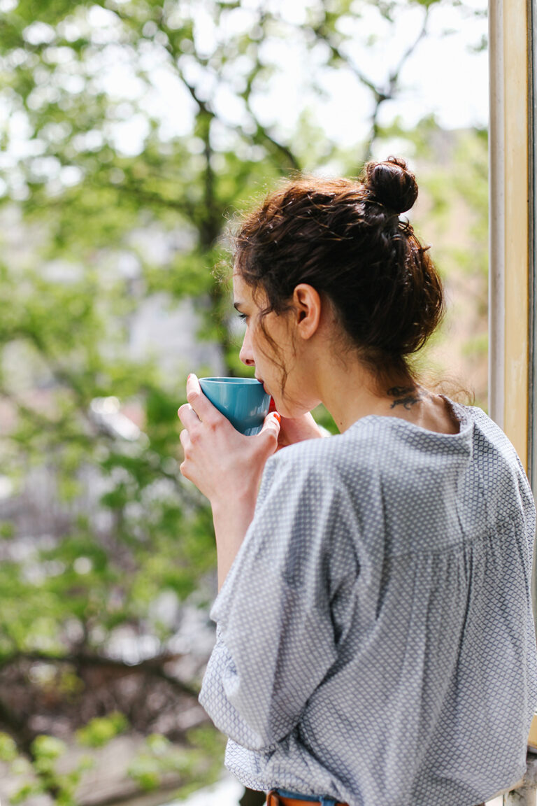 Junge Frau beim entspannten Kaffeetrinken vor einem Fenster